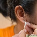 Фото тату: руки аккуратно очищают пирсинг уха ватной палочкой, демонстрируя правильный уход за свежим проколом.