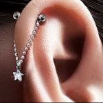 Фото пирсинга уха с серебряной цепочкой, проходящей через хрящ, и звездочкой на конце. Стильный и необычный дизайн для тех, кто любит оригинальность.