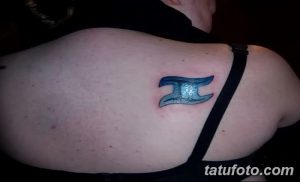 Фото небольшого тату Близнецы на плече. Изображение символа зодиака в синих тонах.