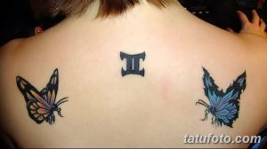 Фотография татуировки на спине девушки, изображающей символ Близнецы и две красочные бабочки, выполненной в ярких цветах.