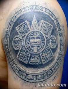 Фото тату календаря ацтеков на плече, выполненное в технике blackwork. Детализированный рисунок с множеством символов и узоров.