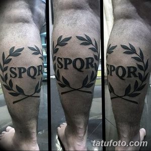 Фото тату с изображением аббревиатуры SPQR, окруженной лавровым венком, на икре мужчины. Черно-белый рисунок татуировки выполнен в четком графическом стиле.