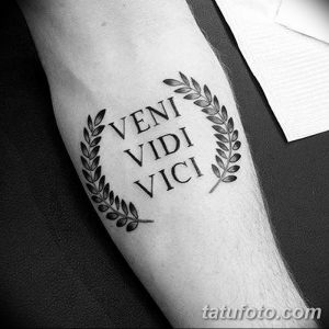 Черно-белое фото татуировки на предплечье с надписью 'Veni Vidi Vici' в лавровом венке. Четкие линии и классический стиль.