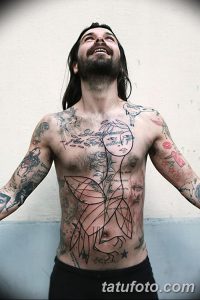 Фотография мужчины с множеством абстрактных татуировок на груди, руках и ногах, смотрящего вверх.