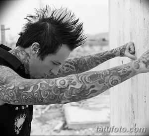 Фото мужчины с длинными волосами и множеством татуировок на шее, руках и теле. Татуировки выполнены в стиле традишнл и изображают различные узоры и символы.