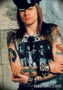 Фото тату Слэша, гитариста Guns N' Roses, с татуировками на предплечьях, включая портрет и символы.