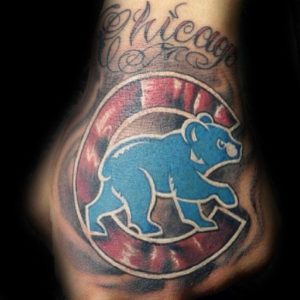 Фото тату на предплечье с логотипом Chicago Cubs и надписью 'Chicago'. Рисунок выполнен в ярких цветах с использованием красных и синих оттенков.
