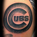 Фото тату с логотипом бейсбольной команды Chicago Cubs на плече. Черно-серый рисунок с трещинами и надписью '2016'.