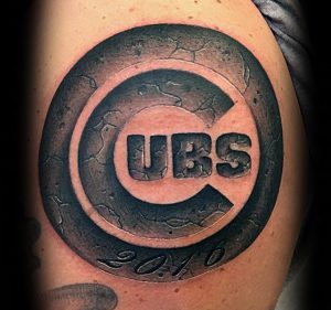 Фото тату с логотипом бейсбольной команды Chicago Cubs на плече. Черно-серый рисунок с трещинами и надписью '2016'.