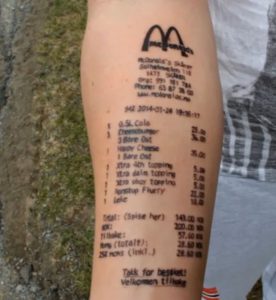 Детализированная татуировка чека из McDonald's на руке. Изображены логотип, дата, список заказанных блюд и итоговая сумма.