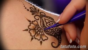 Фото процесса нанесения тату мехенди на кожу, где мастер аккуратно наносит узор с помощью специального инструмента.