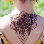 Фото тату мехенди на верхней части спины. Детализированный цветочный узор, напоминающий кружево, выполнен в технике росписи хной.