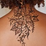 Фото тату мехенди на затылке и верхней части спины. Изящный цветочный узор, выполненный в коричневых тонах, с тонкими линиями и деталями.