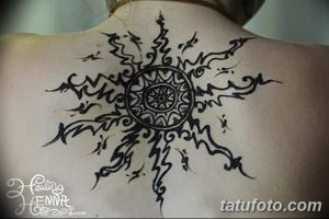 Фото тату хной на спине, изображающее стилизованное солнце с лучами. Четкий контур и детализированный центр делают этот рисунок привлекательным.