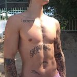Фото тату: Джастин Бибер демонстрирует татуировки на груди, руках и шее, позируя на фоне зелени.