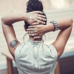 Фото тату на спине и руках певицы. Видны геометрические узоры и абстрактные элементы. Оригинальный образ в светлой одежде.