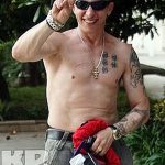 Фото тату на теле мужчины: рукава с рисунками, грудь с иероглифами. Мужчина показывает жест победы и улыбается.