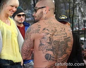 Фото татуировки на спине мужчины. Череп, микрофон, надписи, черно-серые тона, детализированная проработка.