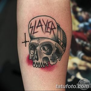 Фото тату: Череп в кепке с логотипом группы Slayer, выполненный в стиле олд скул на руке.