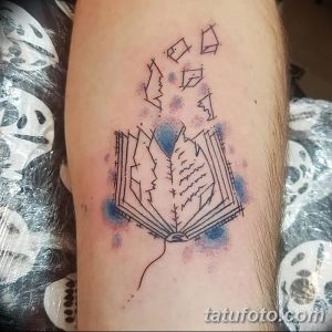 Фото акварельной татуировки на руке с изображением открытой книги, из которой вылетают страницы. Использованы синие и фиолетовые оттенки, создающие эффект легкости и воздушности.