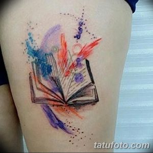 Фото тату на бедре с изображением открытой книги, выполненной в технике акварели. Яркий и красочный рисунок татуировки с размытыми красками.