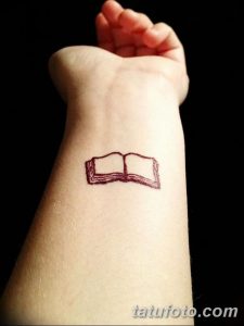 Фото тату: небольшая татуировка на запястье с изображением открытой книги в красных тонах. Простой и элегантный эскиз для любителей чтения.