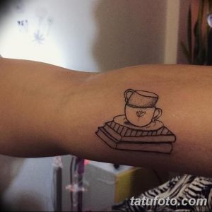 Фото тату с изображением чашки кофе, стоящей на книге, выполненной в черно-белом стиле с небольшими деталями.