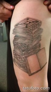Фото тату с реалистичным изображением стопки книг на руке, выполненной в технике черно-белой татуировки с использованием теней и полутонов.