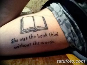 Фото тату с изображением открытой книги и цитаты 'She was the book thief without the words' на предплечье, выполненной в стиле минимализм.