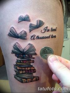 Фото тату на руке: стопка книг, летящие страницы и цитата "I've lived a thousand lives". Черно-белый рисунок татуировки.