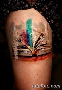 Фото акварельной тату на плече: открытая книга с яркими мазками краски. Красочный и абстрактный рисунок татуировки.