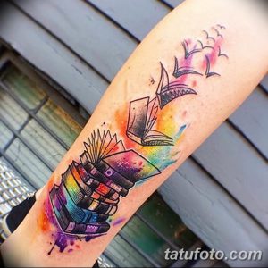 Фото акварельной татуировки на предплечье: стопка книг, из которой вылетают бумажные кораблики. Использованы яркие цвета и плавные переходы.