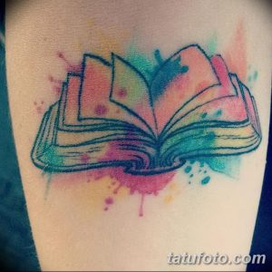 Фото тату: акварельная татуировка с изображением открытой книги. Яркие розовые, голубые и зеленые цвета, размытые контуры.