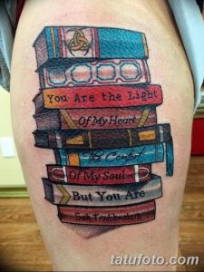 Фото тату на ноге: Стопка книг с цитатами, украшенная цветами и узорами. Цветная татуировка, детализированный стиль.