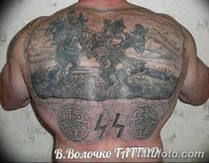 Фото тату на спине: масштабный рисунок с изображением кавалерийской атаки, символики и элементов пейзажа. Черно-серые тона, детализированная проработка.