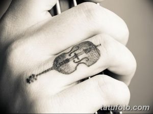 Фото миниатюрной татуировки скрипки на пальце руки. Черно-белый рисунок татуировки с высокой детализацией.