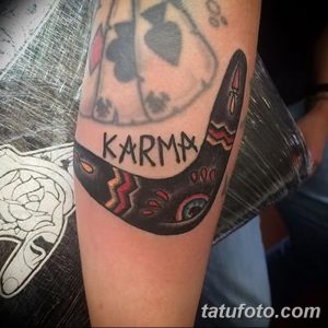 Фото тату бумеранга с надписью 'KARMA' на руке. Традиционный стиль, яркие цвета, четкие контуры. Идея для татуировки.
