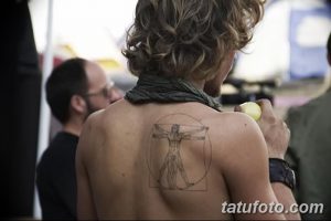 Фото татуировки на спине мужчины, изображающей Человека Витрувиана в круге. Черно-белая татуировка с четкими линиями и детальной прорисовкой.