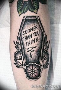Фото тату на ноге: черно-белый рисунок с гробом, украшенным надписью 'Sooner Than You Think' и цветами, выполненный в минималистичном стиле.