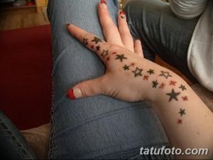 Фото тату: множество маленьких звезд разных цветов на руке и пальцах. Яркий и красочный рисунок татуировки в стиле акварель.