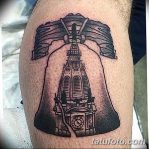 Фотография черно-серой татуировки на ноге, изображающей колокол свободы с трещинами и детальной проработкой. Реалистичный и стильный дизайн.