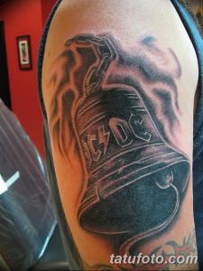 Фото тату колокольчика AC/DC с огненным эффектом. Черно-серые тона, реализм, динамичный дизайн.