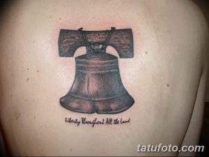 Фото татуировки колокола с надписью "Liberty Throughout All the Land". Черно-серый рисунок тату, расположен на спине.