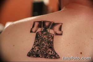 Фото татуировки колокола, корпус которого заполнен изображениями черепов. Черно-белый рисунок тату, расположен на лопатке.
