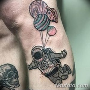 Небольшая татуировка на руке с изображением космонавта, держащего планеты, как воздушные шары. Рисунок выполнен в черно-белой гамме с добавлением серых оттенков.