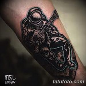 Фото тату: космонавт, играющий на гитаре, выполненный в стиле blackwork. Черные линии, контрастные тени, динамичная композиция.