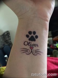 Фото тату с изображением отпечатка кошачьей лапы и надписью 'Oliver' с сердечком. Небольшой рисунок татуировки на запястье.