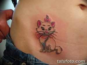Фото тату котенка с розовым бантиком на животе, выполненное в мультяшном стиле. Небольшой рисунок татуировки на боку.