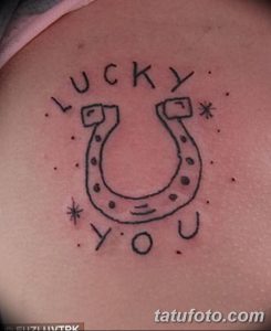 Фото тату: минималистичная татуировка подковы с надписью 'LUCKY YOU', выполненная в черном цвете на коже.