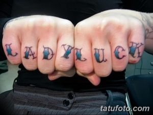 Фото татуировки с надписью 'Lady Luck' на костяшках пальцев. Черные чернила, классический шрифт, минималистичный дизайн.